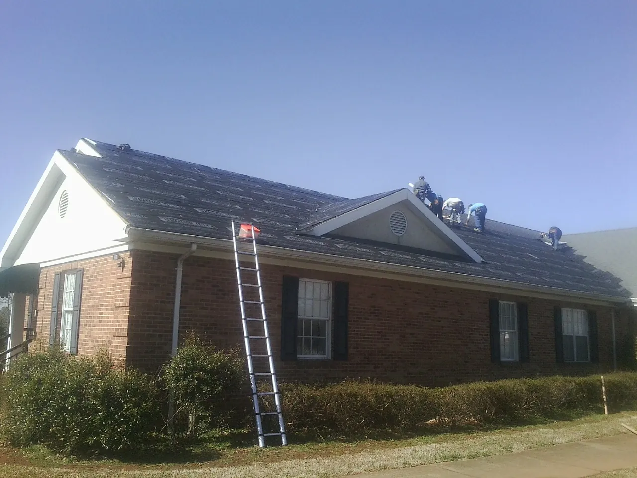 Crew tearing shingles off a brick ranch roof with a ladder set — Metal Roof Repair work by our crew in Signal Hill