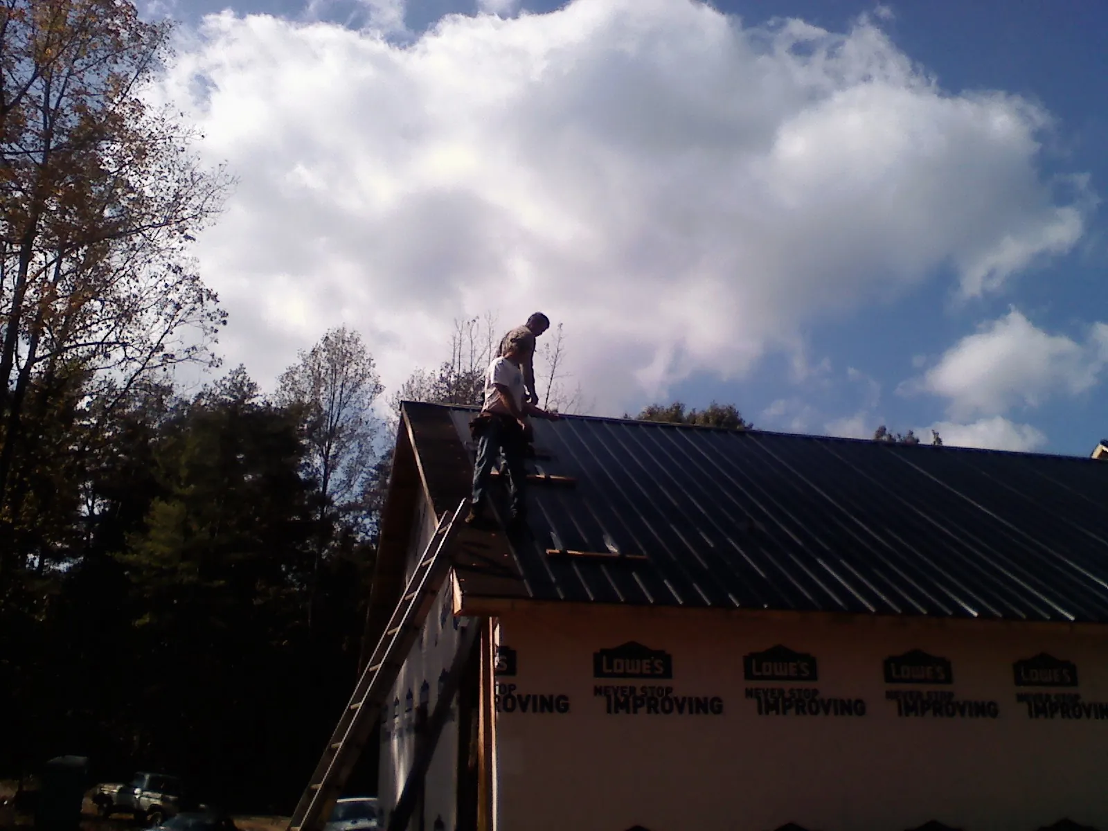 Roofer fastening dark metal panels high against a cloudy sky, from a Roof Inspection job in Signal Hill