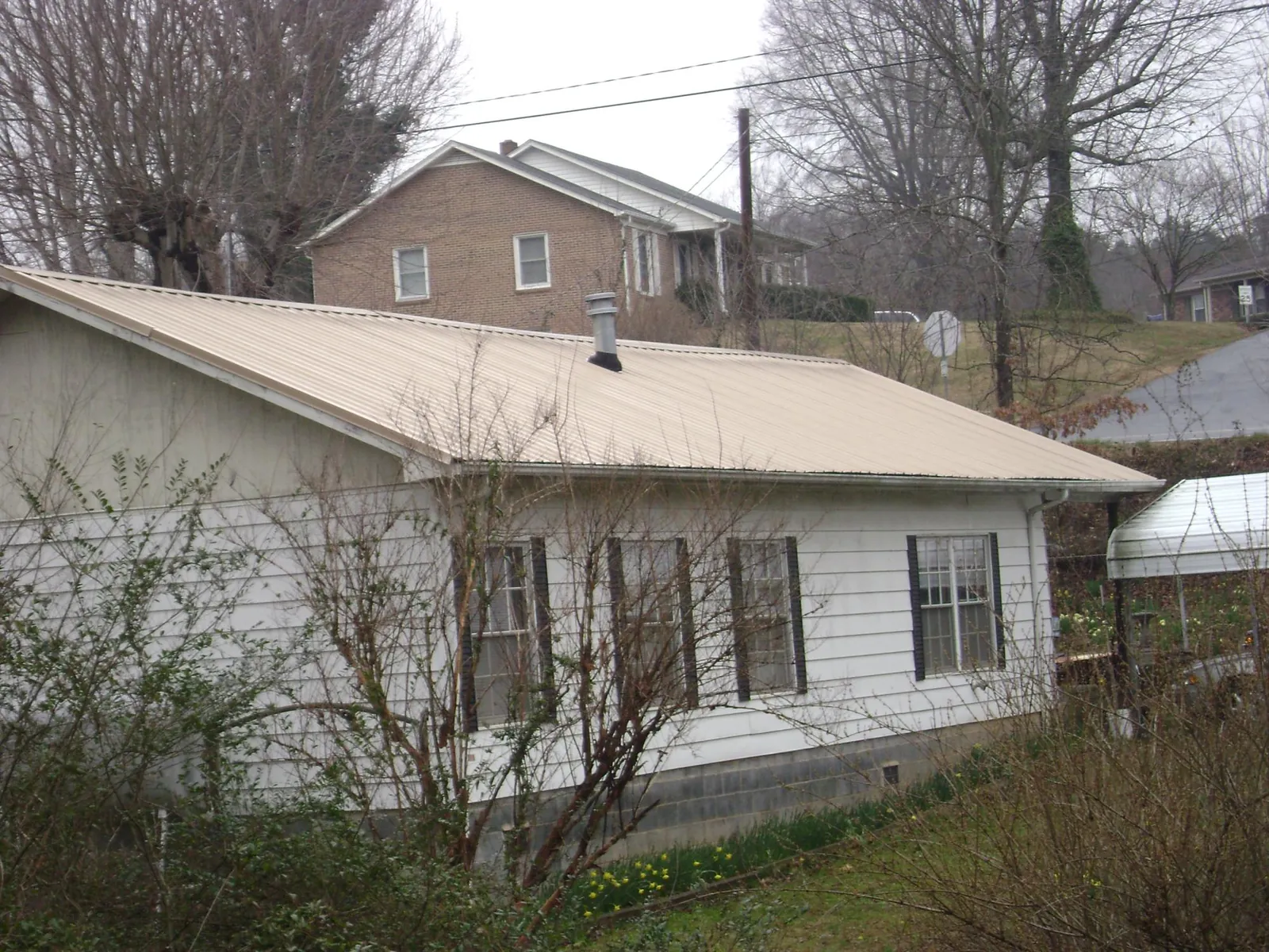 Tan metal roof on a white sided house set into a hillside — Commercial Roofing by Roofing Brothers in Signal Hill